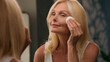 © Yuliia - Beautiful middle-aged 50s old lady mature woman applying powder luxury cosmetics on face with cotton pad perfect smooth skin natural makeup in mirror home bathroom facial wrinkles anti-aging beauty