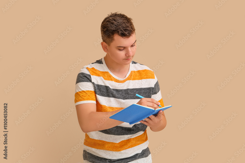 Teenage boy writing something in notebook on beige background