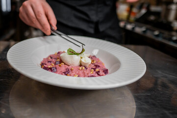 Wall Mural - A chef delicately garnishes a vibrant beetroot risotto topped with a creamy burrata cheese and pine nuts, showcasing culinary artistry in a modern kitchen setting