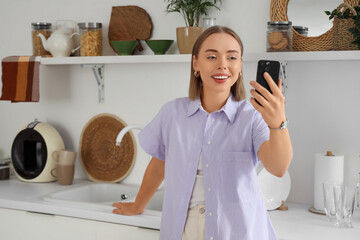 Canvas Print - Young woman with mobile phone video chatting in kitchen