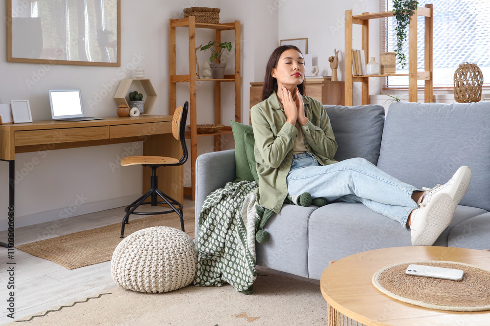 Young Asian woman self-examining thyroid gland on sofa at home