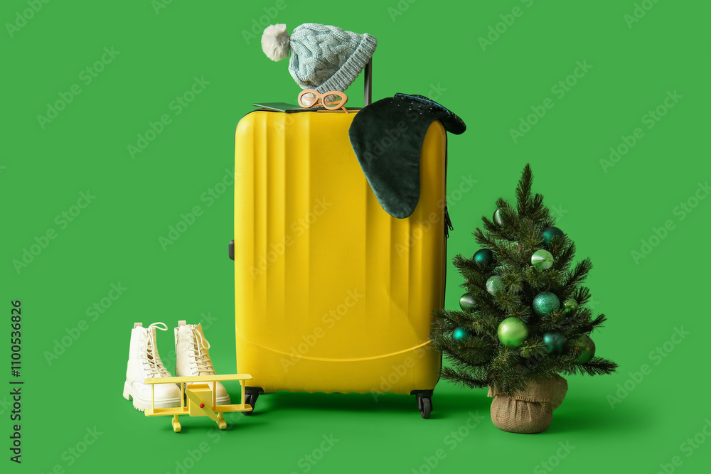 Suitcase with Christmas tree and  travel accessories on green background