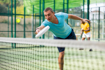 Wall Mural - Sporty european man padel tennis player trains on the outdoor court using a racket to hit the ball