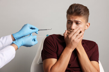 Wall Mural - Dental phobia. Dentist working with scared man on grey background, closeup