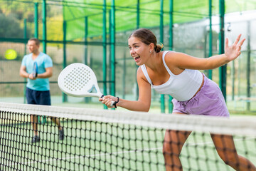 Wall Mural - Sporty emotional young woman padel tennis player trains on the outdoor court using a racket to hit the ball