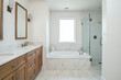 © Nyetock - A bathroom with a natural wood cabinet with a white marble countertop, white herringbone tile around the tub, and a walk-in shower with large tiles.