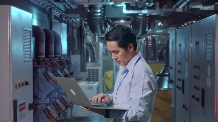 Side View Of An Asian Male Professional Worker Standing With His Laptop In Engine Control Room, Typing On His Laptop'S Keybaord With Meditation