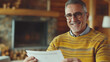 © Dai - Senior man smiling joyfully as he receives a retirement payment check in a cozy living room, celebrating financial security and peaceful home life.