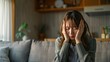 © evgenia_lo - A woman is seated on a couch with her hands on her head, expressing stress and worry in a warm and inviting living space