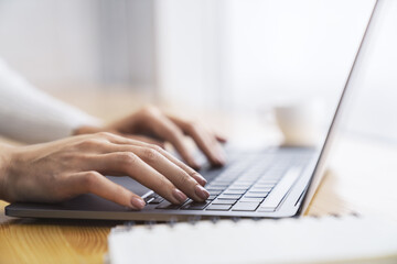 against a blurred office scene, a close-up shot reveals a woman's hands typing on a modern laptop ke
