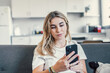 © Daniel - Young beautiful woman sit on sofa in living room using modern smartphone, make call or order at home. Client of e-commerce services, mobile application usage. Technology, connection, lifestyle concept