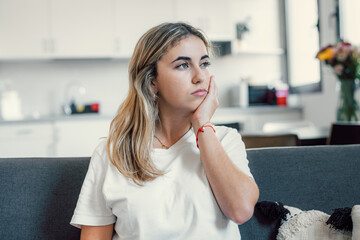 Wall Mural - Side view young woman looking away at window sitting on couch at home. Frustrated confused female feels unhappy problem in personal life quarrel break up with boyfriend or unexpected pregnancy concept