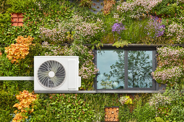 Air-source heat pump on a green sustainable building covered with blooming vertical hanging plants