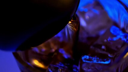 Wall Mural - Close-up of a dark liquid being poured into a glass with ice cubes, showing a rich, smooth drink under blue lighting. 4k Video footage