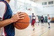 © SerPak - A basketball player stands with the ball in hand, observing teammates practice shooting in a gym. The setting is lively with players engaged in various drills, demonstrating teamwork and skill develop