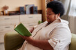 © Seventyfour - Side view portrait of African American senior woman reading book sitting on couch and enjoying relaxing day at home copy space