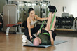 © DragonImages - Female fitness trainer helping elderly man with resistance bands exercise on gym mat, emphasizing focus and technique indoors modern fitness facility