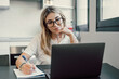 © Daniel - Millennial blonde girl sit at desk in living room study on laptop making notes, concentrated young woman work on computer write in notebook, take online course or training at home, education concept.