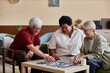 © Seventyfour - Group of elegant senior people playing board game together enjoying quiet entertainment indoors in cozy living room
