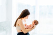 © Iryna - Mother holding newborn baby in sunlit room with soft light