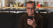 © Oleksii - Elderly caucasian male person, glasses to read a message on smartphone screen. At home, living room.