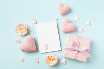 Wall Mural - Festive background for Valentine or Mothers Day. Empty paper card, hearts, rose flowers and gift box on blue table top view.