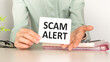© Pawel - Closeup on business woman holding a card with Scam Alert message, business concept image with soft focus background