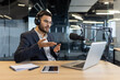 © Liubomir - Man in suit with headphones speaks into microphone during podcast in office. Uses laptop and tablet while communicating effectively. Concept of technology, communication, and media.
