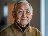 Portrait of an older man with glasses and a warm smile in a neutral setting. Wisdom, community, and senior lifestyle concepts
