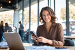 © BOTAHRY DEX - Young Indian business woman manager ceo using cell phone mobile app laptop. Smiling Latin Hispanic mature female businesswoman holding smartphone in office trading, reading, working online. Copy space