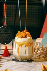 Glass of creamy caramel latte topped with honeycomb pieces on a marble table