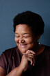 © Seventyfour - Vertical close up portrait of senior African American woman smiling kindly looking down on blue background