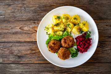 Wall Mural - Fried meatballs, boiled potatoes, beetroots and fresh vegetables served on white plate on wooden table