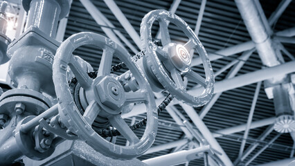 Poster - A metal pipe with a white valve in the middle of it. The valve is attached to a chain and is surrounded by a white metal casing. The pipe is located in a building