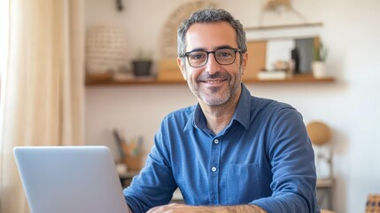 Wall Mural - Man with glasses in a blue shirt working on a laptop at a wooden desk, cozy home office setting with warm light, shelves with decor items blurred in the background, focused work environment