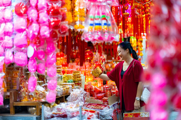 Wall Mural - Happy Asian senior woman celebration Chinese lunar new year festival. Elderly retired woman in red blouse holding shopping bag walking and buying home decorative ornaments at Chinatown street market.