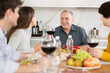 © JackF - Happy senior man celebrating birthday with wife and adult children over cozy family dinner table served with wine and light snacks..
