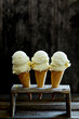 © The Picture Pantry - three ice cream cones filled with vanilla ice cream in a wooden ice cream stand on a dark wooden background