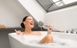 © Prostock-studio - Woman Singing Taking Bath With Foam, Having Fun Holding Shower Head Like Microphone Relaxing In Modern Bathroom Indoor. Cheerful Female Enjoying Bathing With Eyes Closed At Home