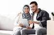 © Prostock-studio - Beautiful middle-eastern couple sitting on couch with digital pad, happy arab man husband and wife woman in hijab moving to new house, buying furniture and electronics online via tablet, copy space