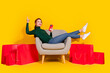 © deagreez - Full length photo of cheerful lucky lady dressed green jumper relaxing chair modern device empty space isolated yellow color background