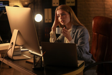 Tired female programmer with cup of coffee working in office at night