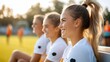 © LifeMedia - A young athlete smiles while sitting on a bench, her ponytail catching the sunlight, depicting joy and energy in the sports setting with teammates nearby.