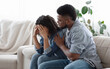 © Prostock-studio - Dependent Relationship Concept. Young Black Guy Soothing His Depressed Girlfriend At Home, Embracing Her On Couch In Living Room