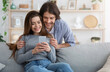 © Prostock-studio - Cheerful couple spending time together at home, watching photos on modern phone, copy space