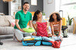 © Pixel-Shot - Happy family sitting on floor and packing suitcase for travel at home