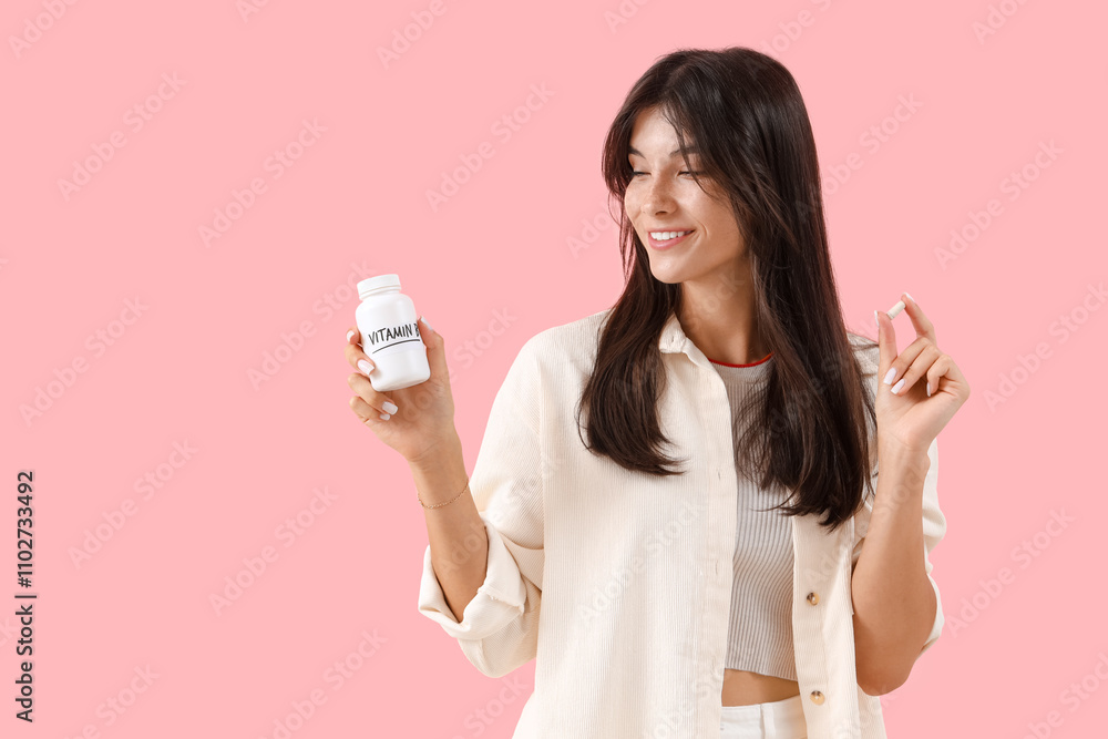 Young woman with vitamin B pills on pink background