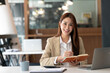 © NAMPIX - Asian businesswoman working with her laptop, calculator and documents in the office., smiling to camera.