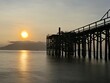 © Neilstha Firman - A weathered wooden pier extends into the water at sunrise, with barnacles clinging to the support posts.