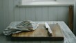 © Kultivad - Wooden cutting board with a knife and a striped cloth on a rustic table, illuminated by soft natural light from a nearby window.